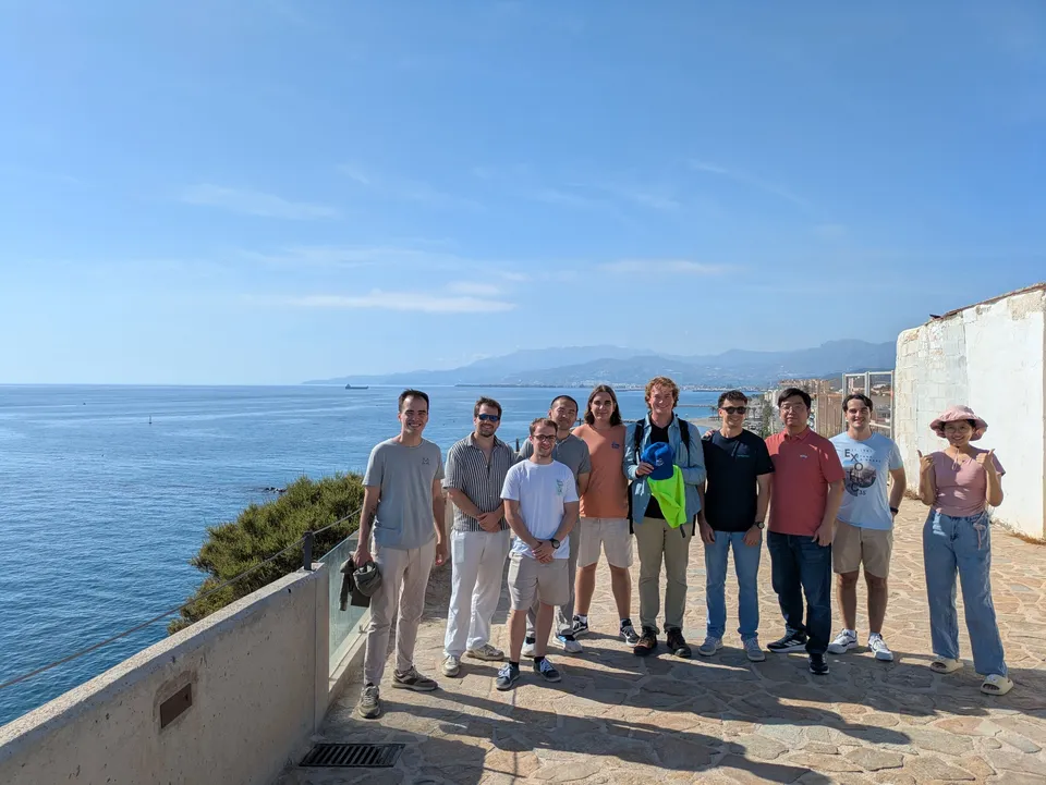 Martin Zoula, in the middle holding something yellow, standing with members of the lab on a seafront terrace