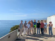 Martin Zoula, in the middle holding something yellow, standing with members of the lab on a seafront terrace